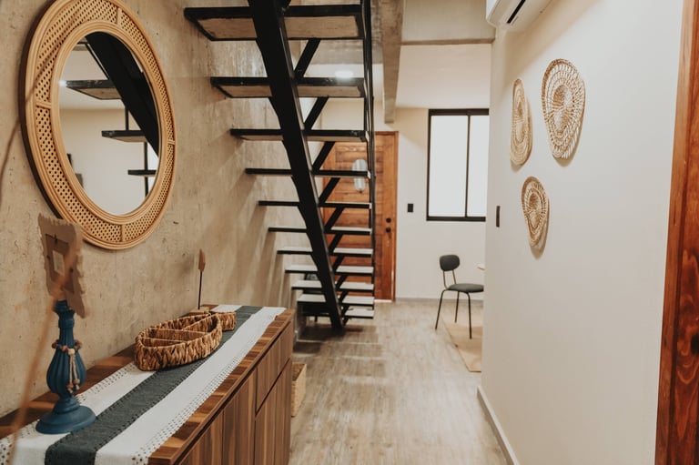 Modern hallway with wooden console table, rattan wall decor, black staircase, and minimalist furnishings.