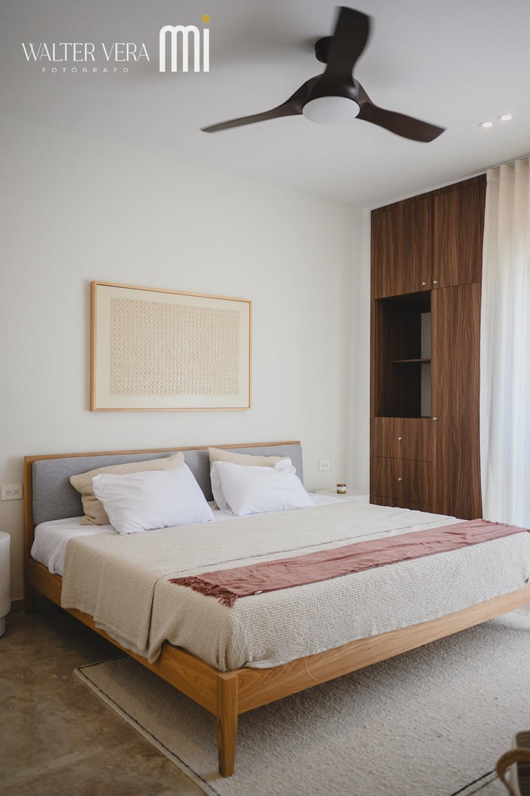 Modern bedroom with wooden platform bed, gray headboard, ceiling fan, wood wardrobe, and framed artwork on white walls