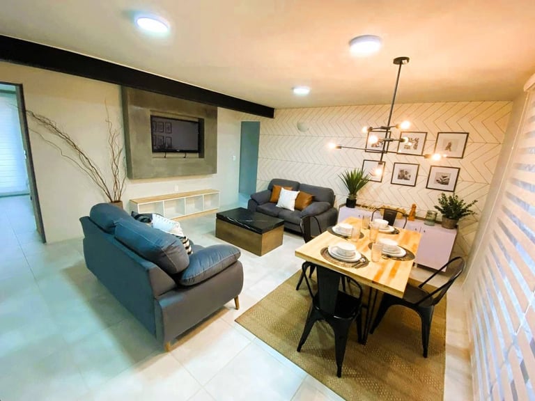 Modern open-concept living room with teal sofa, dining table, wall-mounted TV, and decorative wall art in warm tones