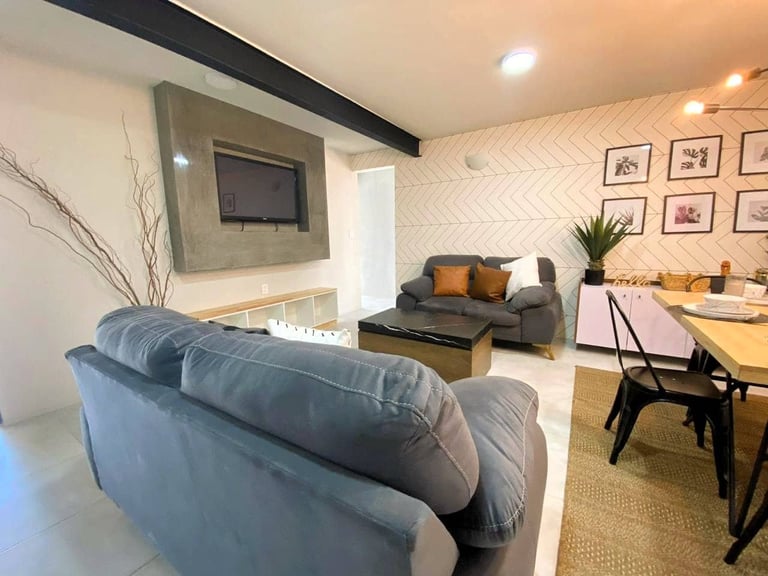 Modern living room with blue sofa, wall-mounted TV, dining area with wooden table, and minimalist decor
