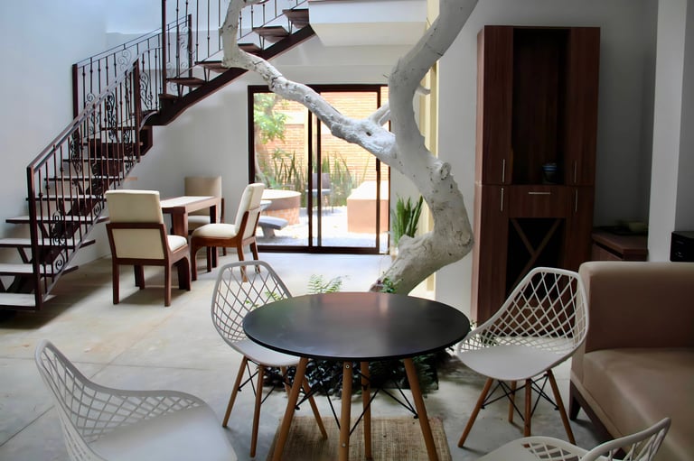 Modern spiral staircase in an open-concept living space with round black table, white chairs, and large windows overlooking a garden