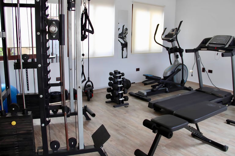 Modern home gym with cable machine, treadmill, elliptical, weight rack, and exercise bench on wooden flooring