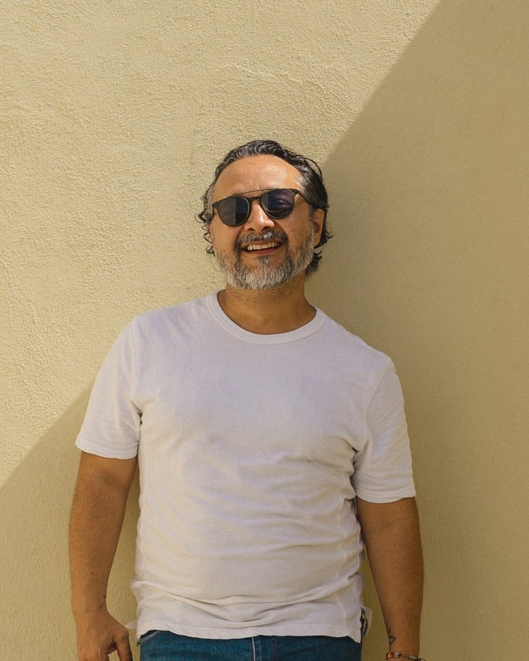 Man wearing sunglasses and white t-shirt standing against a yellow wall