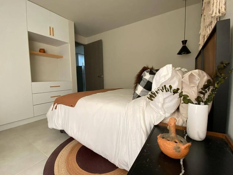 Modern bedroom with white bed, minimalist white storage unit, bedside plants, and pendant light fixture