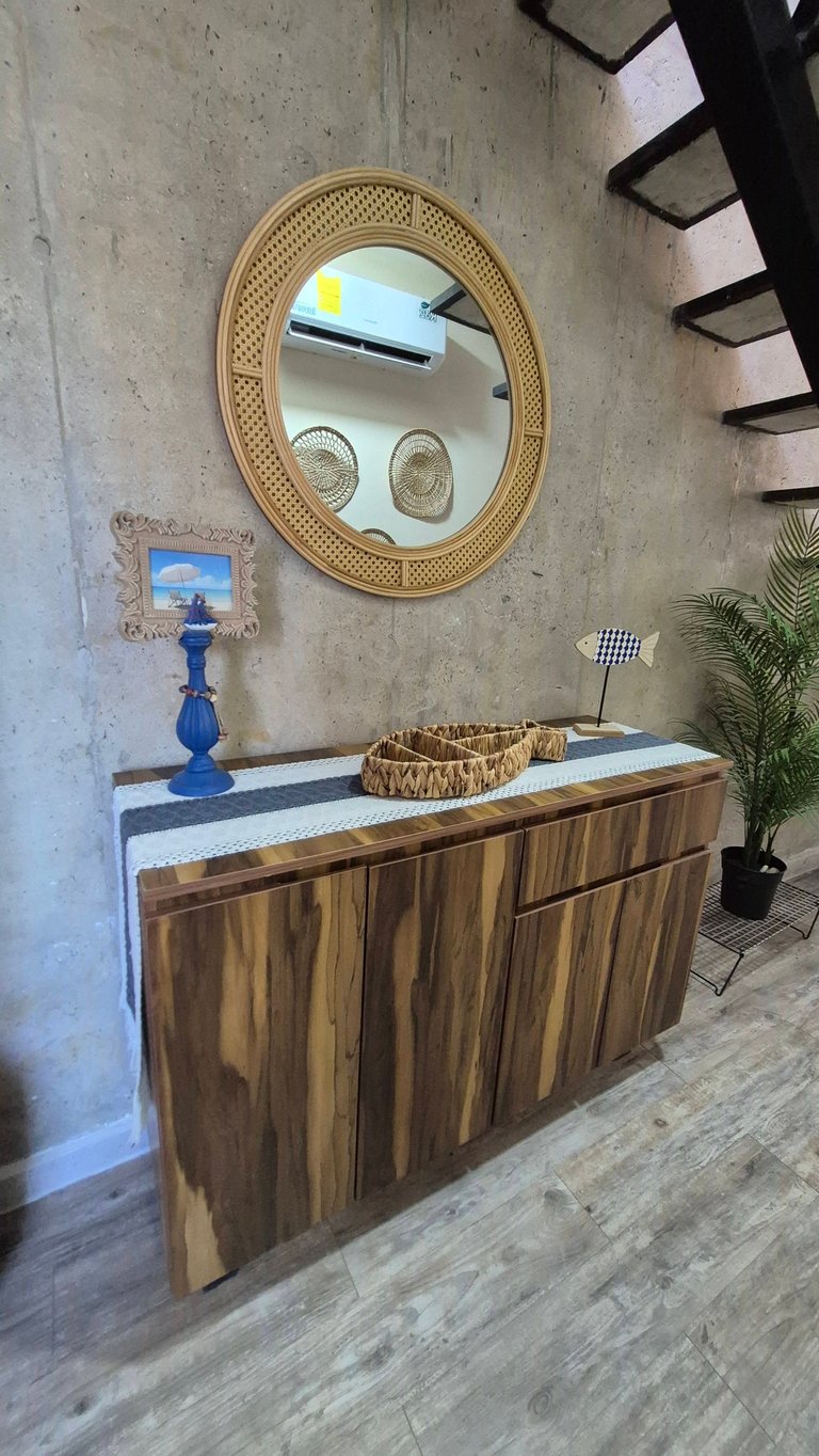 Entryway with wooden cabinet, woven oval mirror, blue pedestal lamp, and decorative accents on a wood-look floor