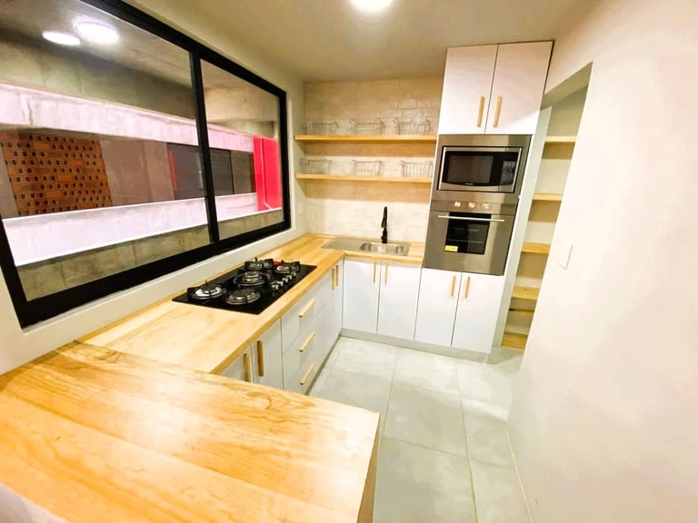 Modern white kitchen with wood countertops, gas cooktop, built-in wall shelves, wall-mounted television, and tiled flooring