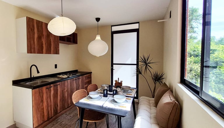Modern kitchen and dining area with wood cabinetry, pendant lights, dining table, and large windows overlooking nature