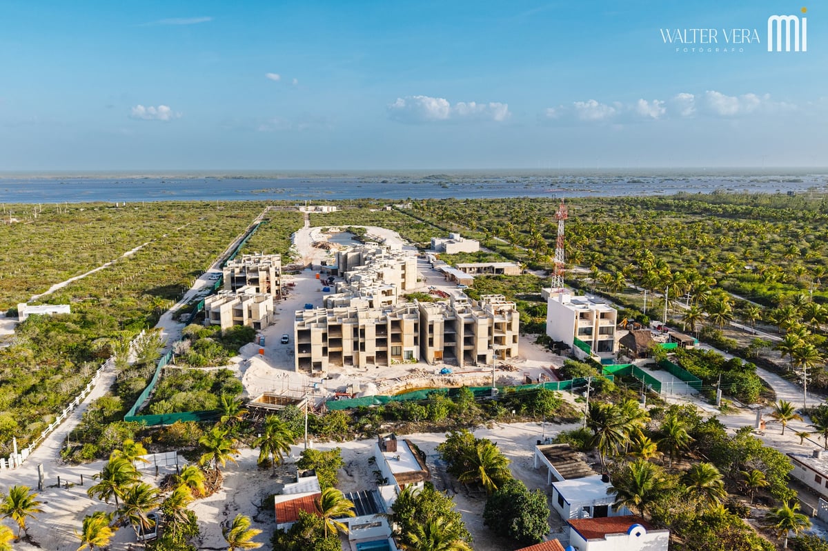 Aerial view of a modern residential complex surrounded by lush vegetation and palm trees, with a lagoon visible in the distance