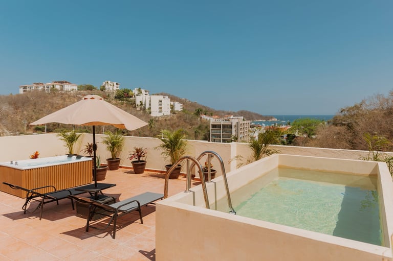 Rooftop terrace with swimming pool, lounge chairs, umbrella, and potted plants overlooking hillside buildings