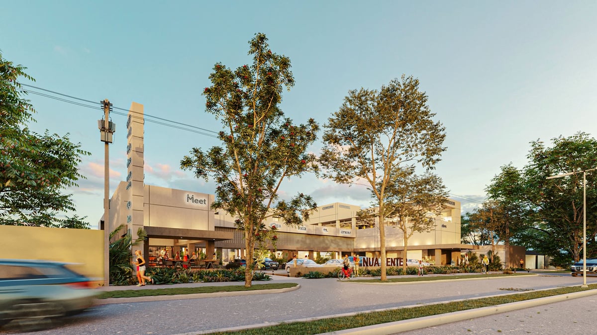 Modern commercial shopping center with beige buildings, tree-lined street, and passing vehicle on sunny day