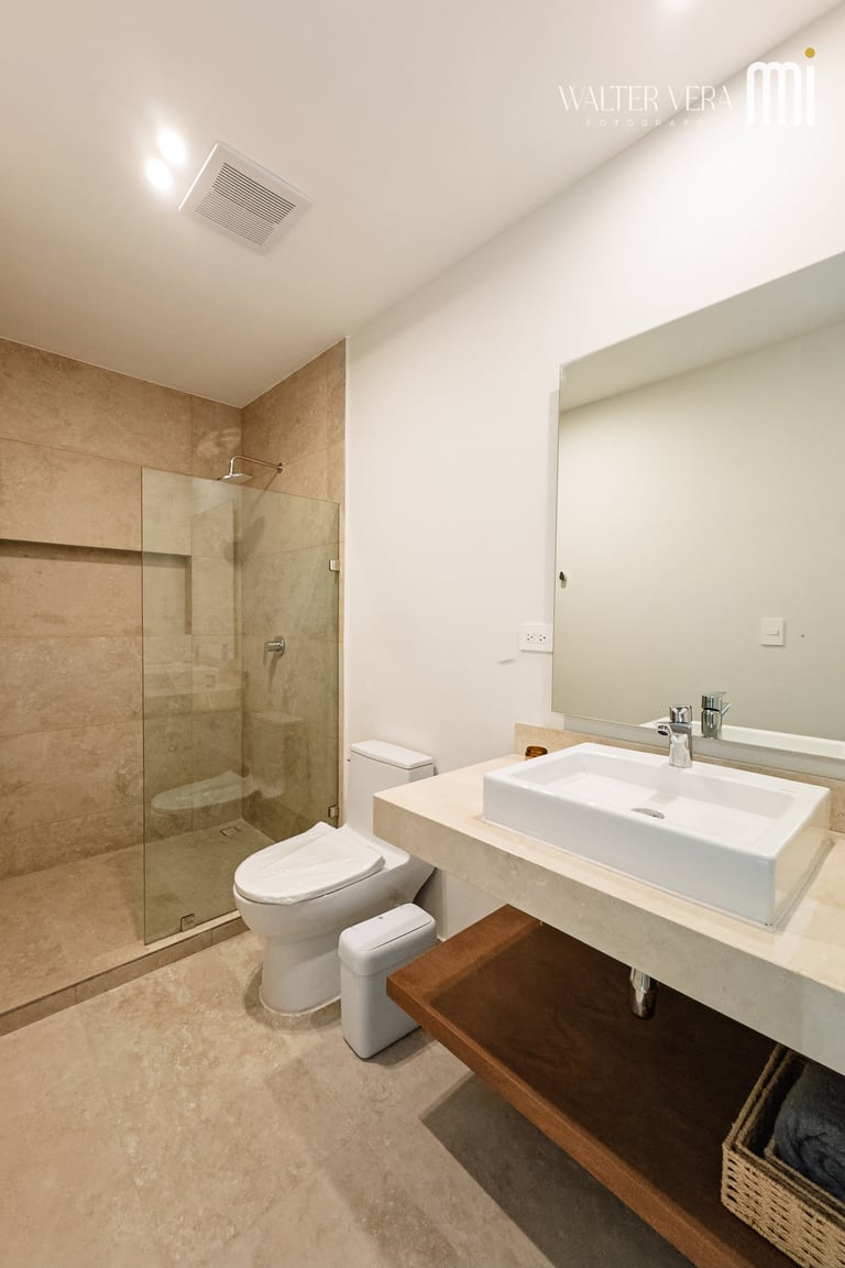 Modern bathroom with beige tile shower, white rectangular sink on floating vanity, toilet, and ceiling recessed lighting