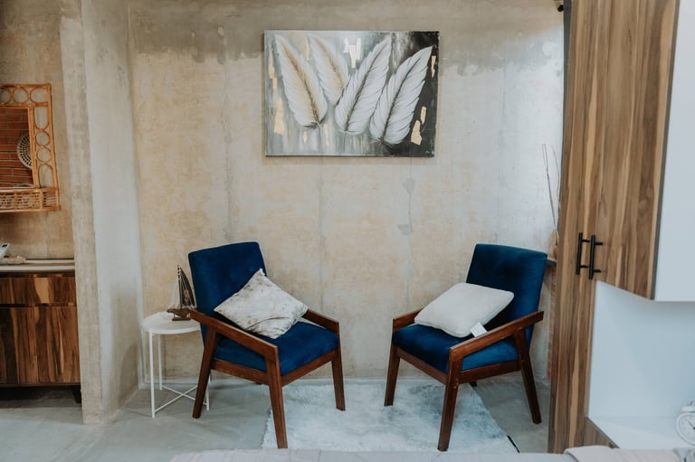 Two mid-century modern chairs with navy blue upholstery and wooden frames positioned facing each other in a minimalist room with abstract wall art