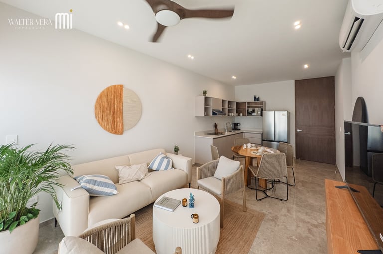 Modern living room with beige curved sofa, wooden round wall art, potted plants, white coffee table