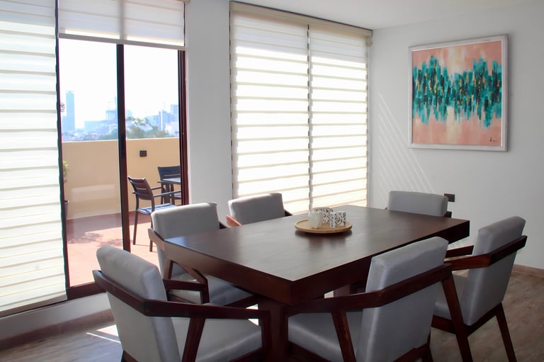 Modern dining room with dark wood table, gray upholstered chairs, sheer window treatments, and abstract artwork on walls.