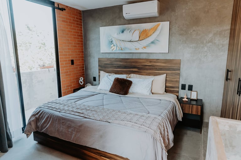 Modern bedroom with queen bed featuring wood headboard, white bedding, exposed brick wall, and minimalist decor